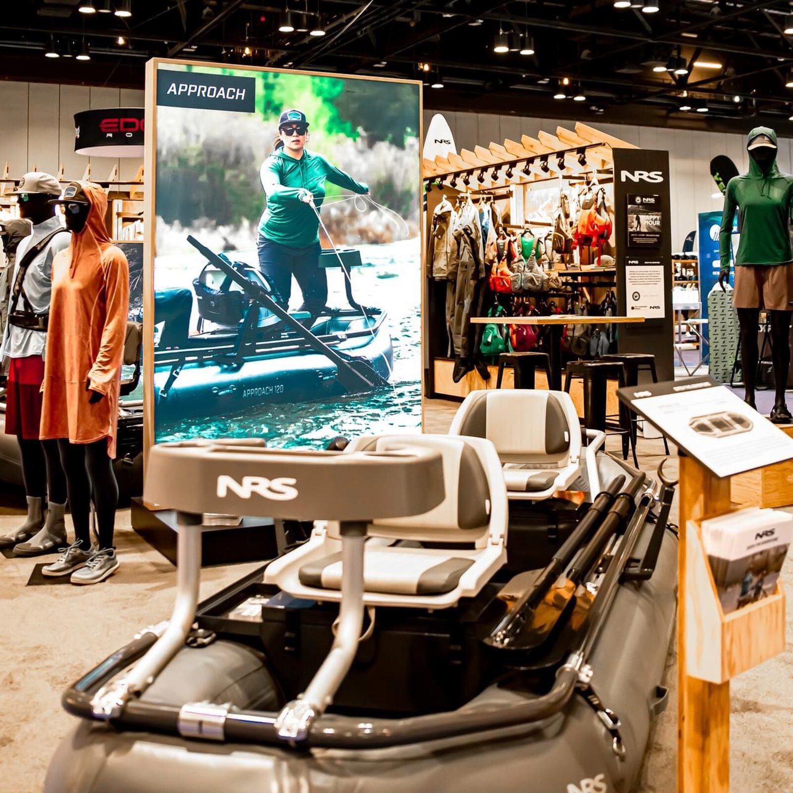 Product-display booth with a tall backlit lightbox graphic and a mannequin apparel wall